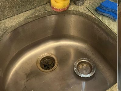 Before: a brushed steel undermount basin with a dulled surface and debris in the strainer.