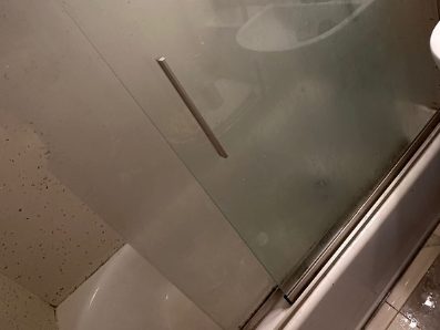 Before: a glass shower screen clouded with soap film so the tub behind it is barely visible.