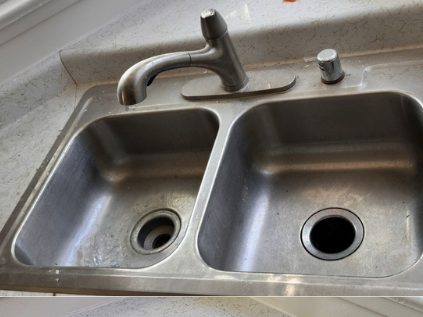 Before: a dull stainless kitchen sink with water marks and dark residue around both drains.