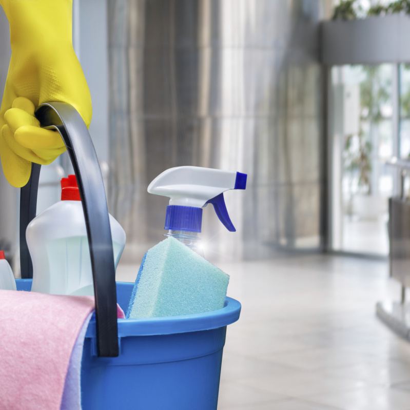 Gloved hand carrying a bucket of cleaning products through a commercial lobby