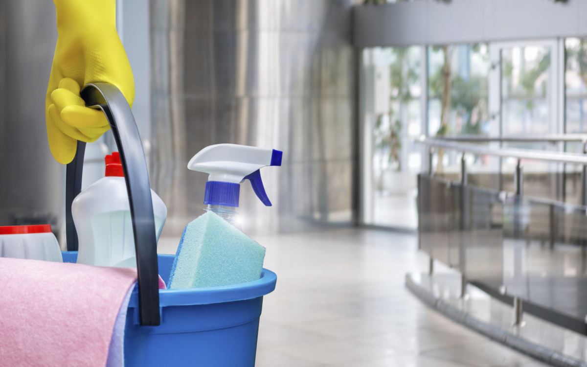 Gloved hand carrying a bucket of cleaning products through a commercial lobby