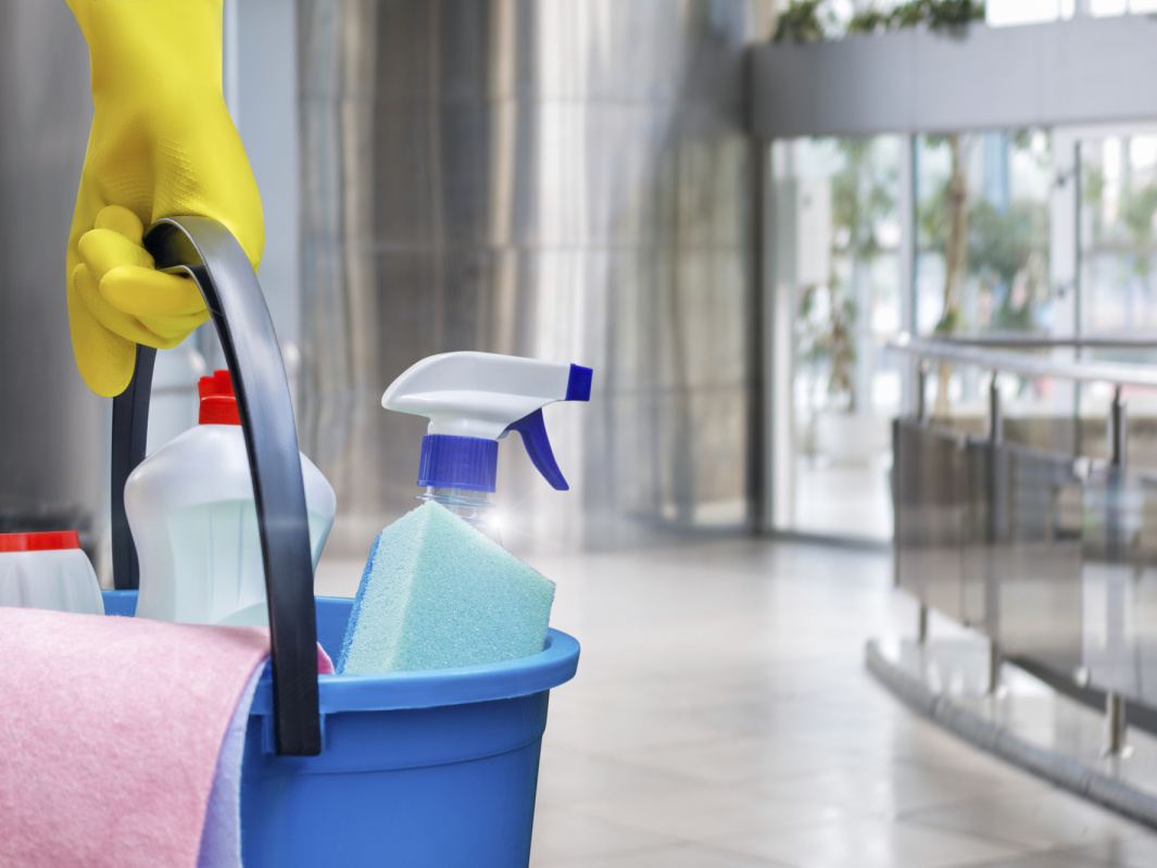 Gloved hand carrying a bucket of cleaning products through a commercial lobby