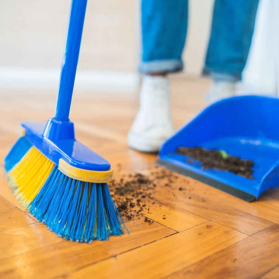 Broom sweeping dirt onto a dustpan on a hardwood floor