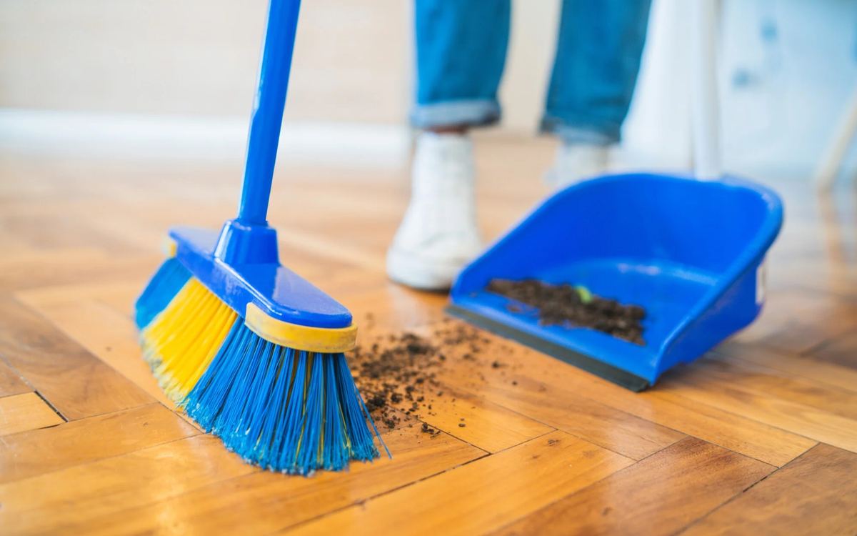 Broom sweeping dirt onto a dustpan on a hardwood floor