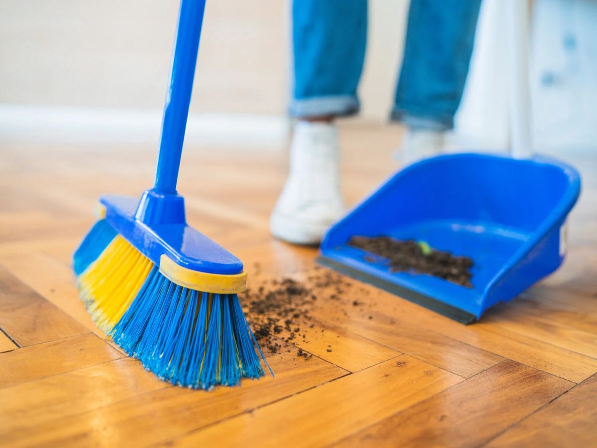 Broom sweeping dirt onto a dustpan on a hardwood floor