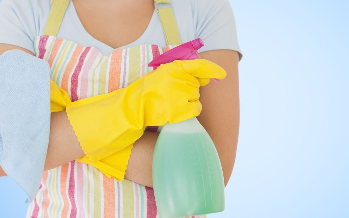 Cleaner in a striped apron and yellow gloves holding a spray bottle and a microfibre cloth