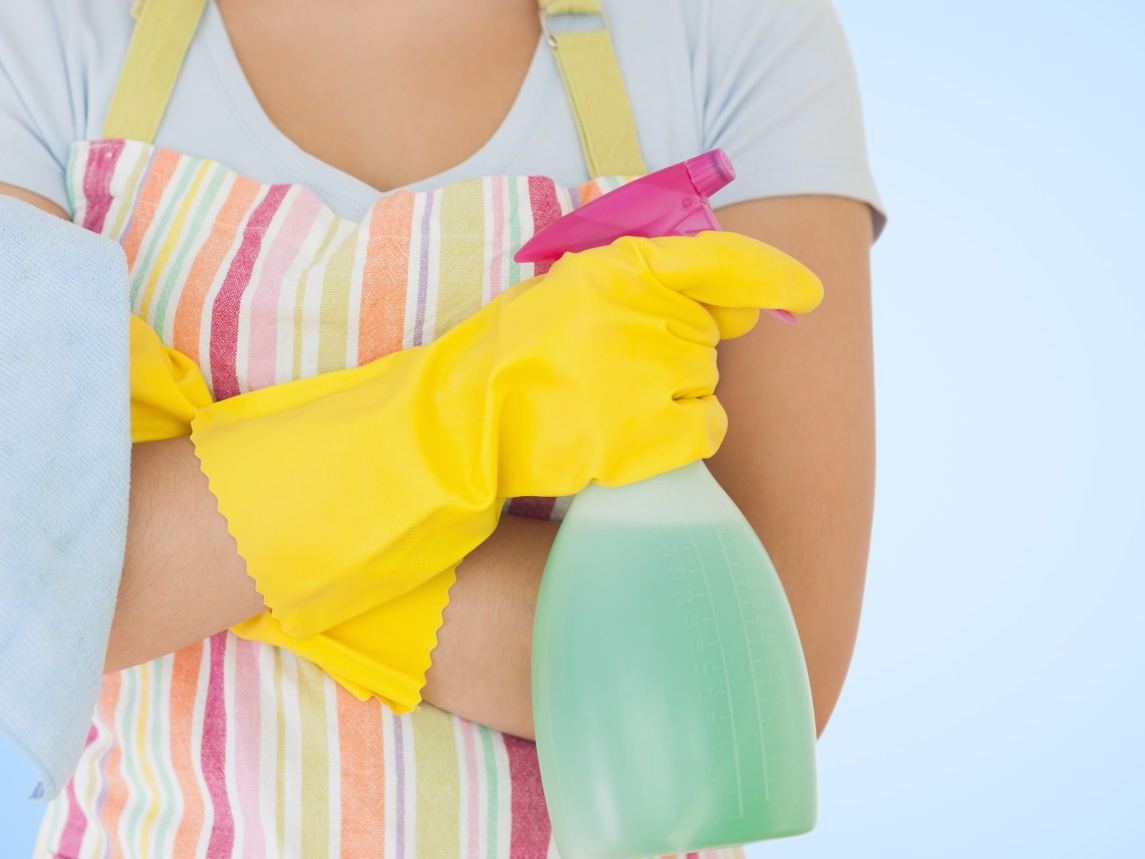 Cleaner in a striped apron and yellow gloves holding a spray bottle and a microfibre cloth