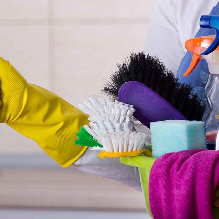 Cleaner giving a thumbs up while holding a caddy of brushes, sponges and spray bottles