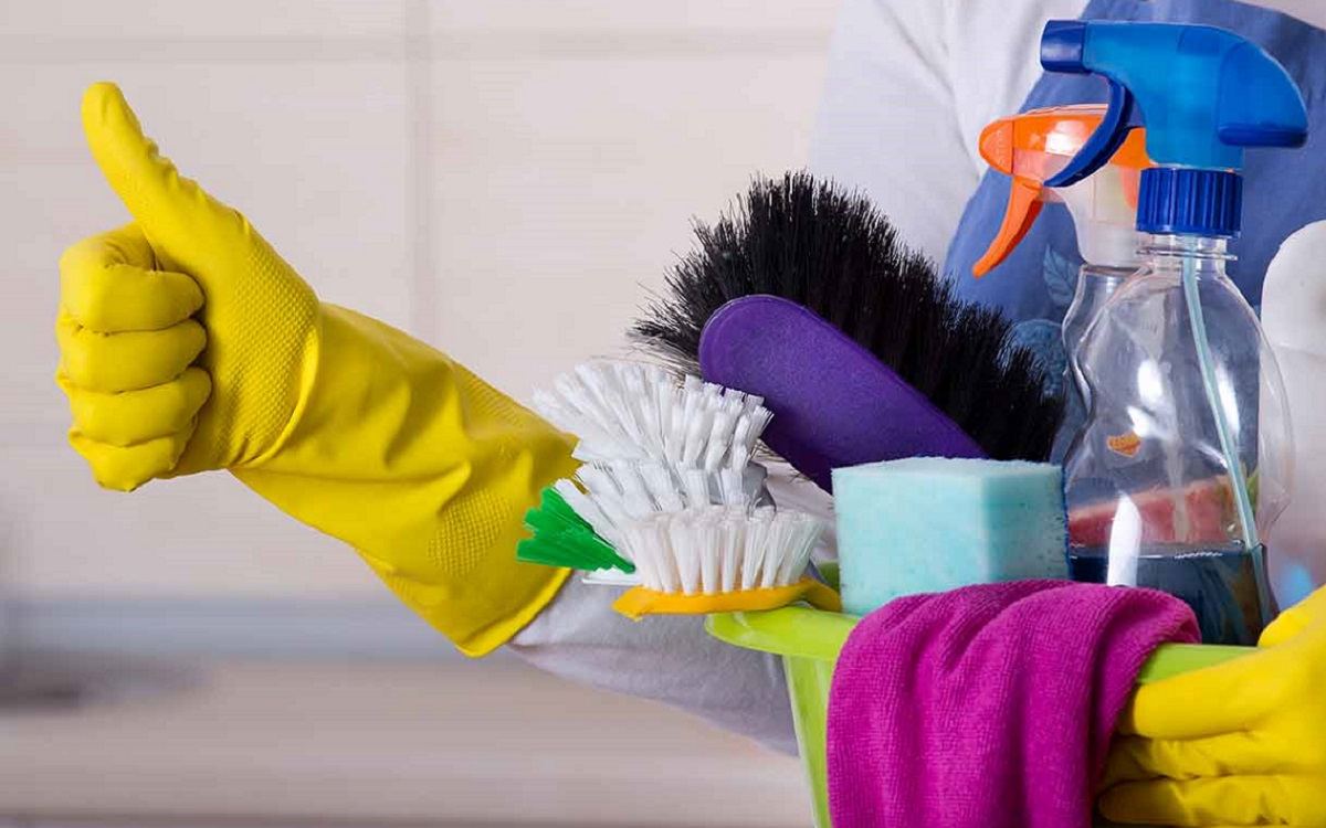 Cleaner giving a thumbs up while holding a caddy of brushes, sponges and spray bottles