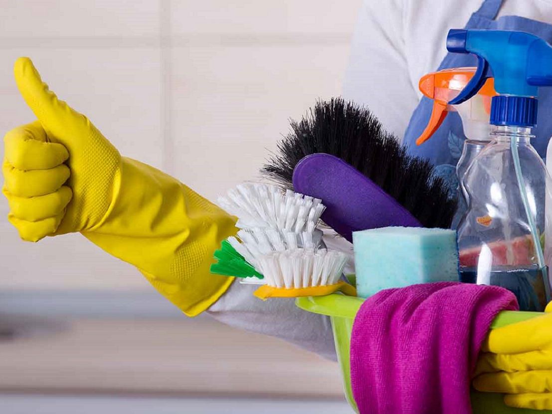 Cleaner giving a thumbs up while holding a caddy of brushes, sponges and spray bottles