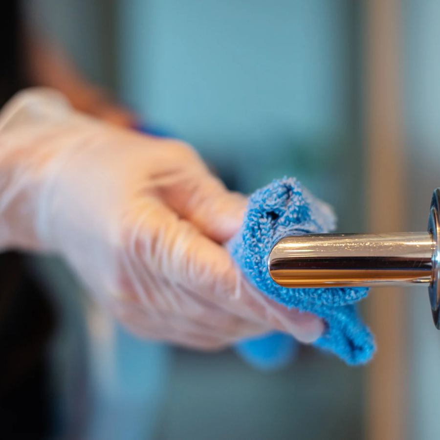 Gloved hand wiping a chrome door handle with a blue microfibre cloth