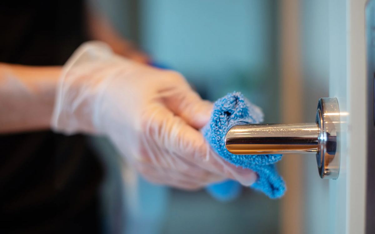 Gloved hand wiping a chrome door handle with a blue microfibre cloth