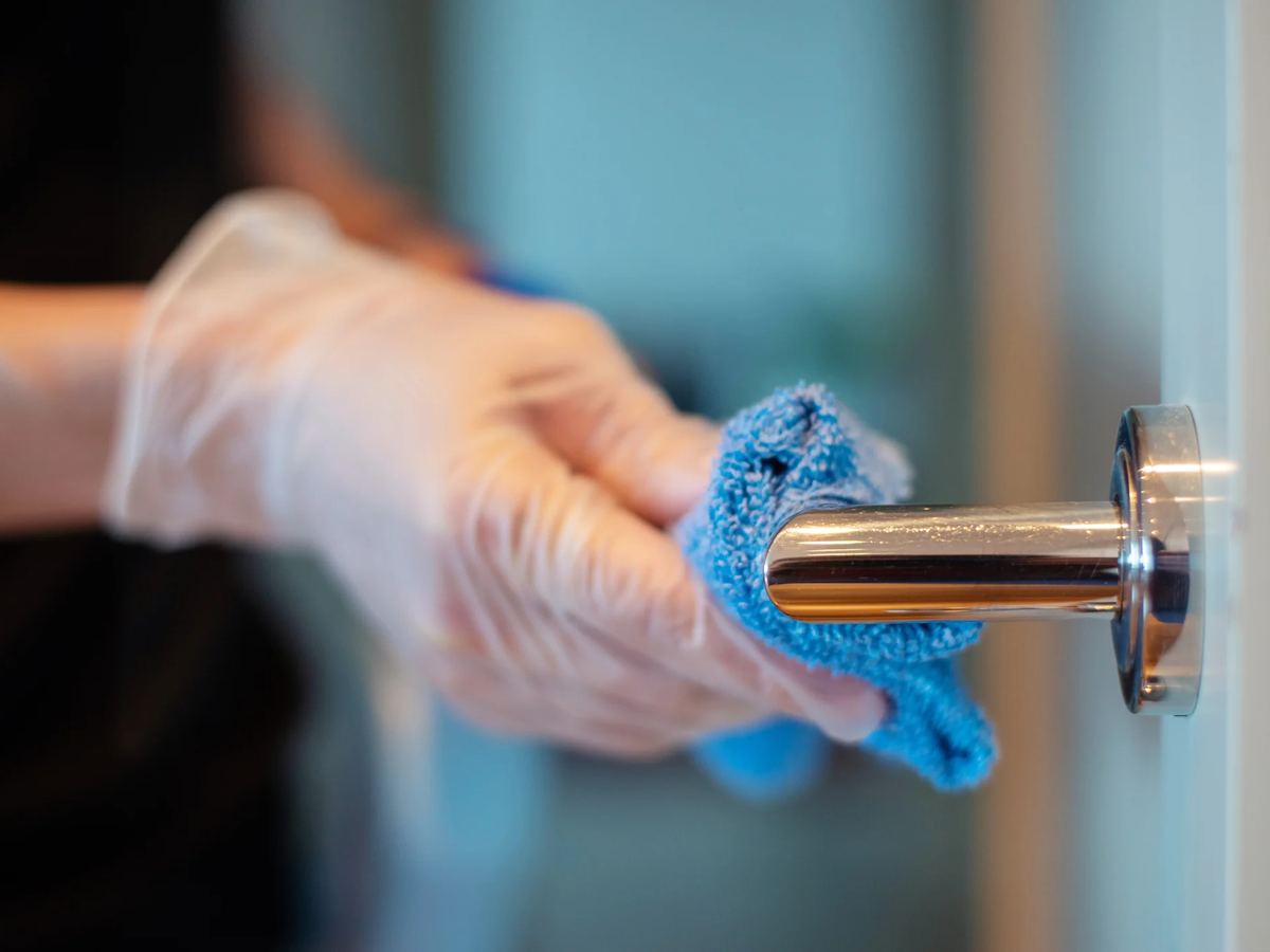 Gloved hand wiping a chrome door handle with a blue microfibre cloth