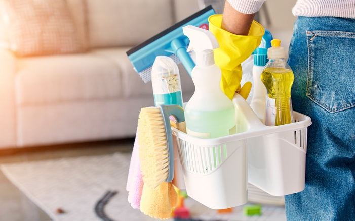 Caddy of cleaning supplies carried into a living room with a sofa and a rug