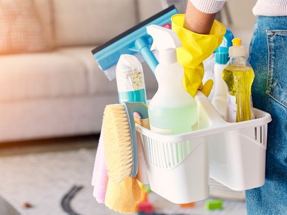 Caddy of cleaning supplies carried into a living room with a sofa and a rug