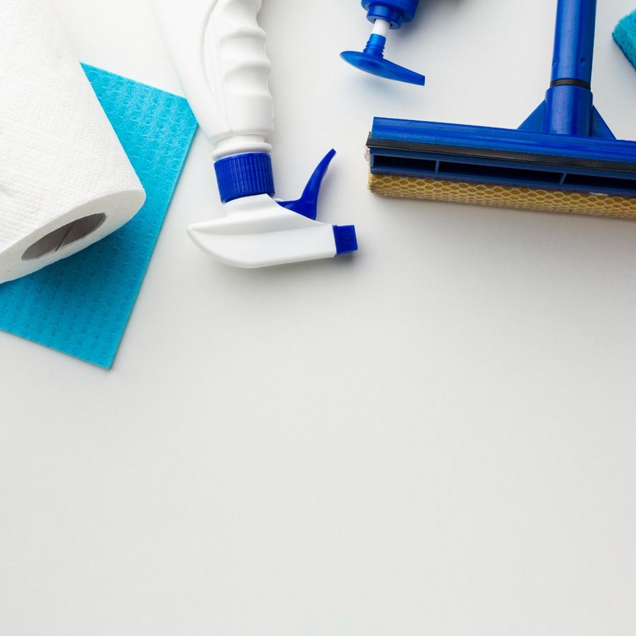 Paper towel, squeegee, sponge and cleaning bottles arranged on a white surface
