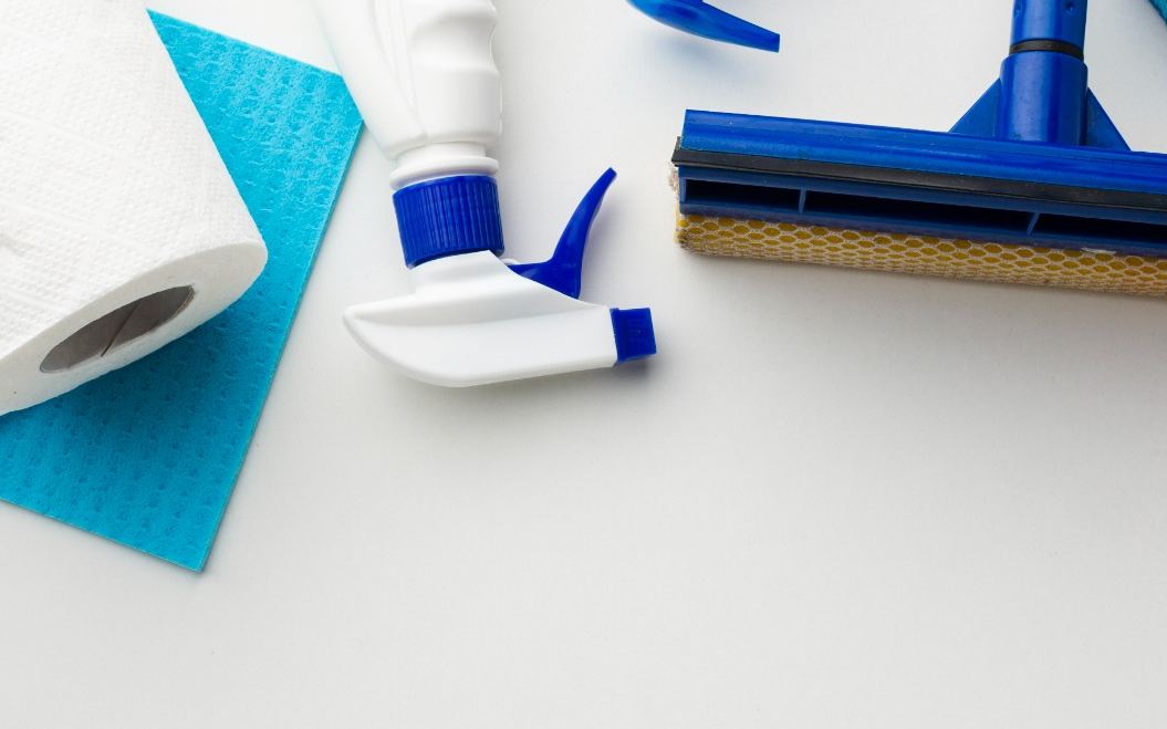 Paper towel, squeegee, sponge and cleaning bottles arranged on a white surface
