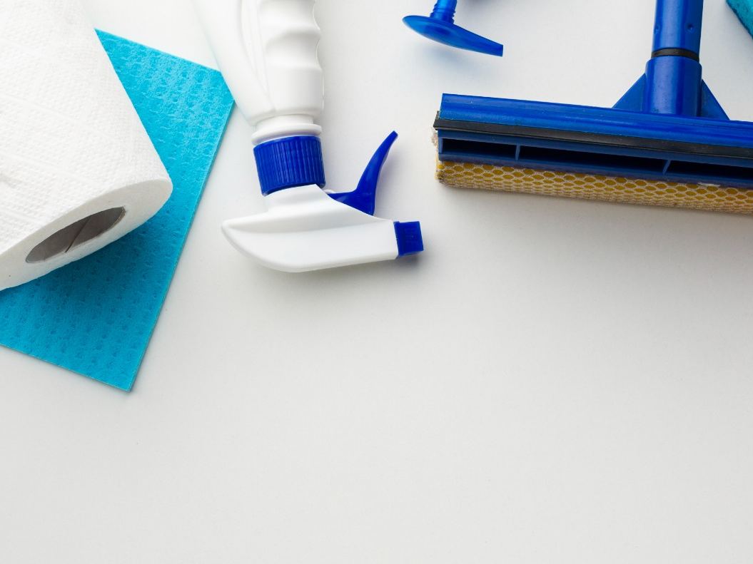 Paper towel, squeegee, sponge and cleaning bottles arranged on a white surface