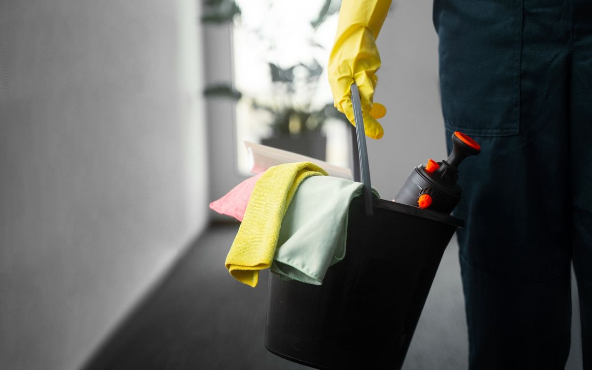 Gloved hand carrying a bucket of colour-coded microfibre cloths down a hallway