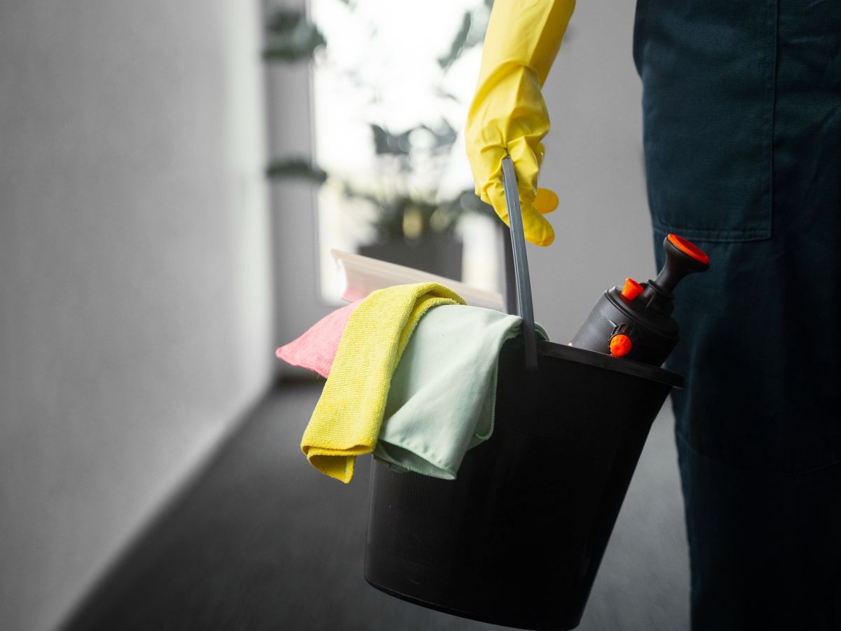 Gloved hand carrying a bucket of colour-coded microfibre cloths down a hallway