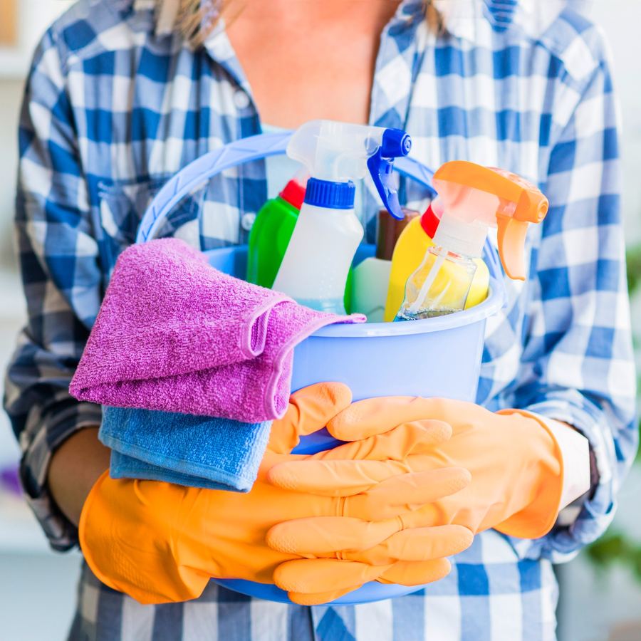Cleaner holding a bucket of spray bottles with folded microfibre cloths