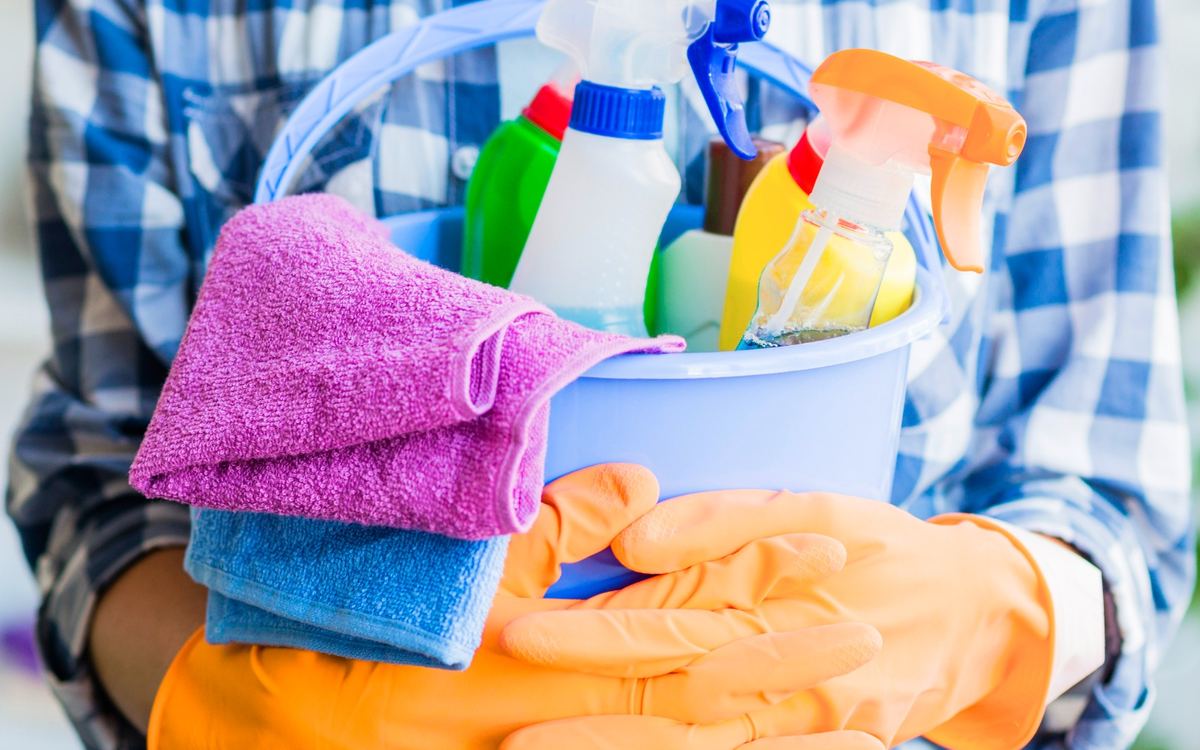 Cleaner holding a bucket of spray bottles with folded microfibre cloths