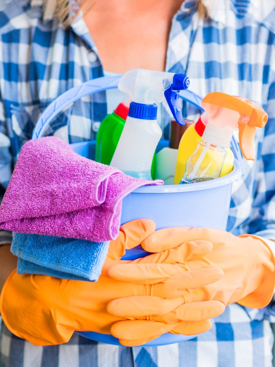 Cleaner holding a bucket of spray bottles with folded microfibre cloths