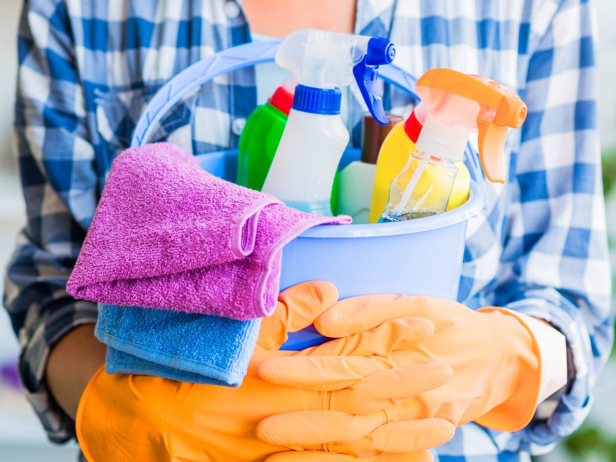 Cleaner holding a bucket of spray bottles with folded microfibre cloths