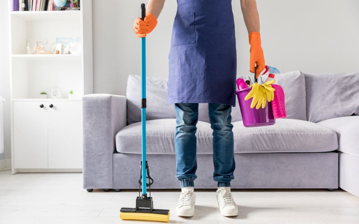 Cleaner with a mop and a bucket of supplies standing in a living room