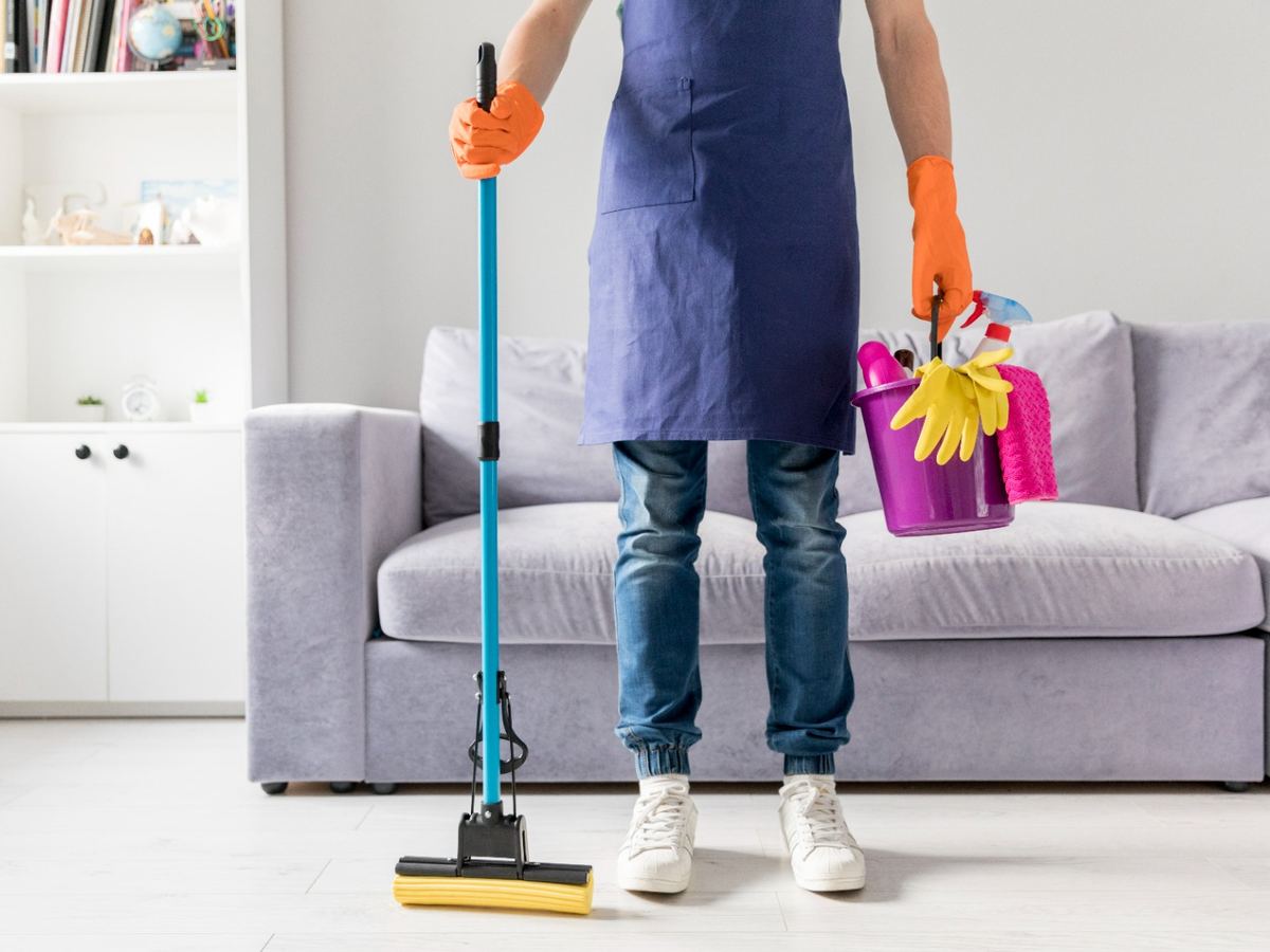 Cleaner with a mop and a bucket of supplies standing in a living room