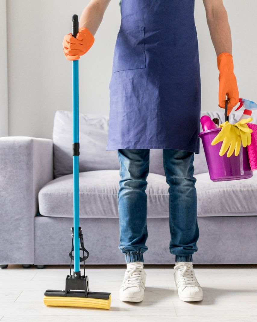 Cleaner with a mop and a bucket of supplies standing in a living room