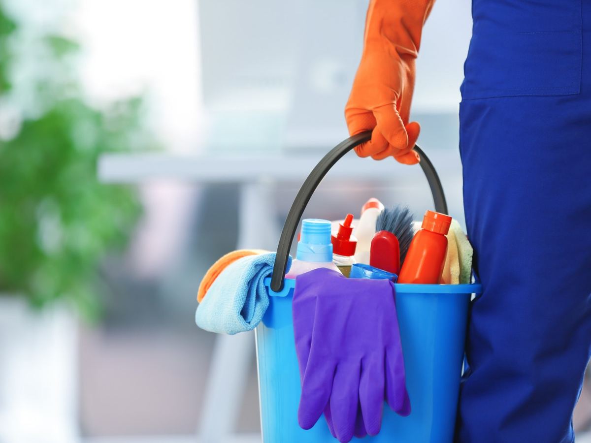 Gloved hand carrying a bucket of cleaning products into an office